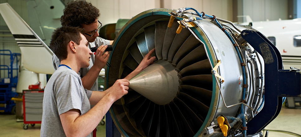 Zwei junge Männer arbeiten an einer Flugzeugturbine in einer Werkshalle
