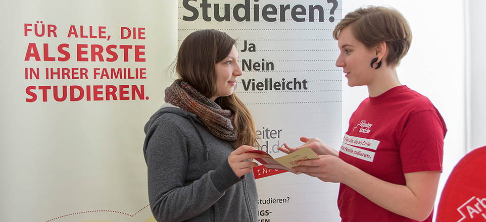 Zwei Menschen unterhalten sich. Im Hintergrund Werbeschrift