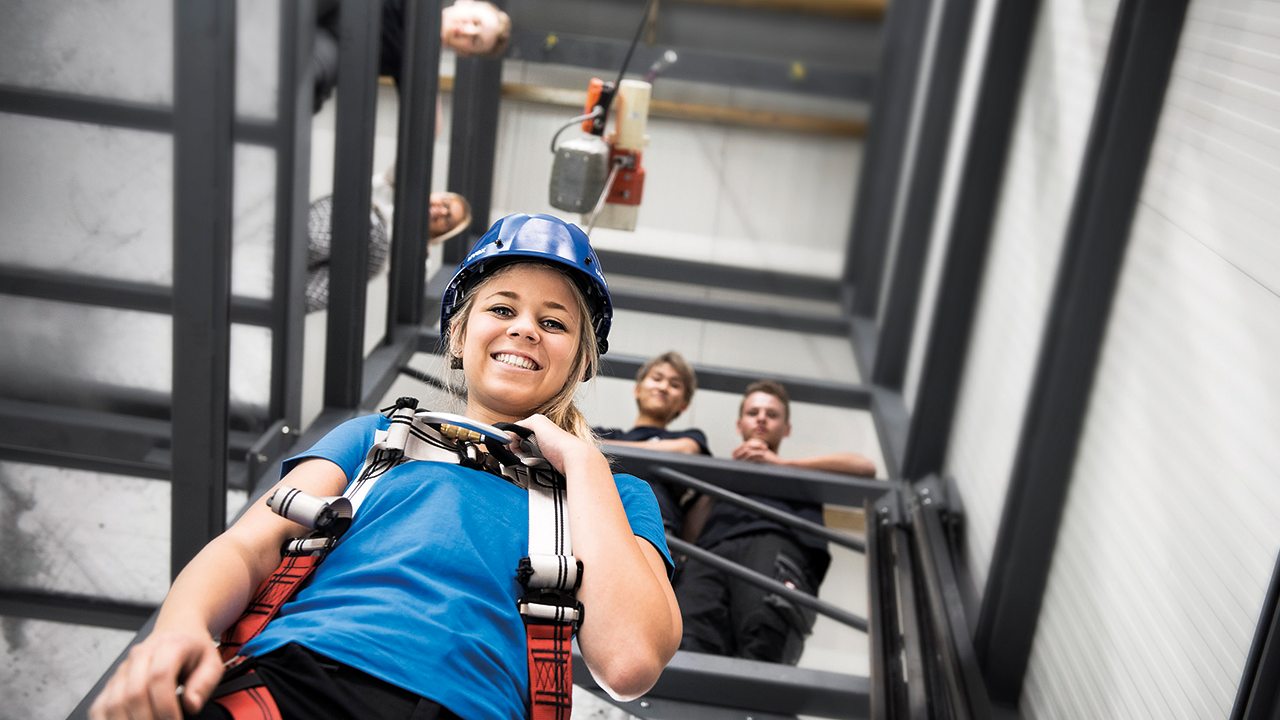 Junge Frau in Kletterausrüstung von unten in einem Schacht fotografiert. Im Hintergrund oben im Schacht stehen weitere Personen.