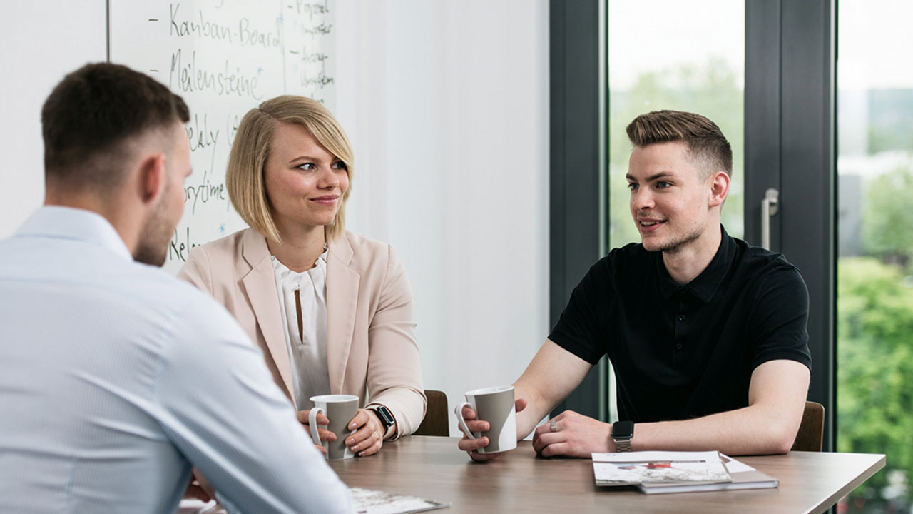 Drei Personen in einer Besprechung, auf dem Tisch Kaffeetassen