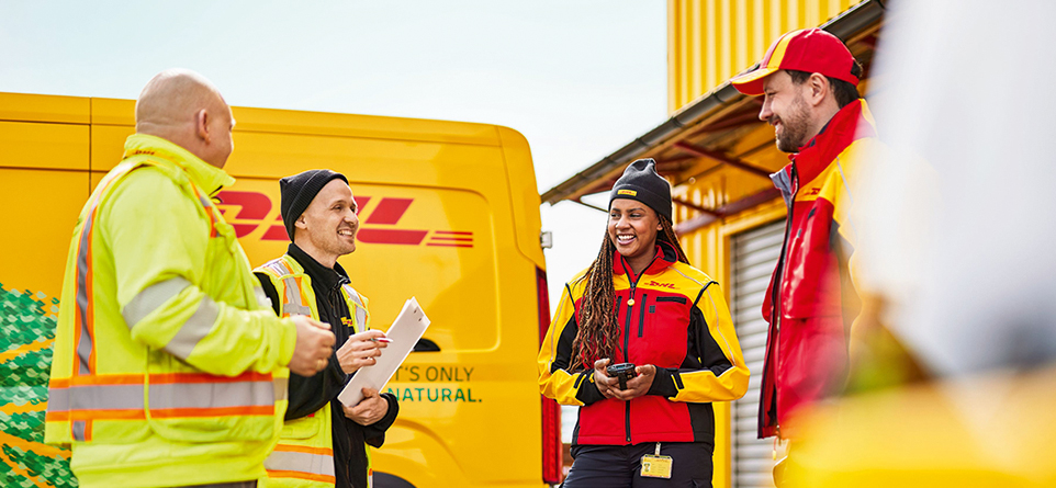4 Mitarbeitende, die sich am Verteilzentrum besprechen, im Hintergrund steht ein DHL Fahrzeug