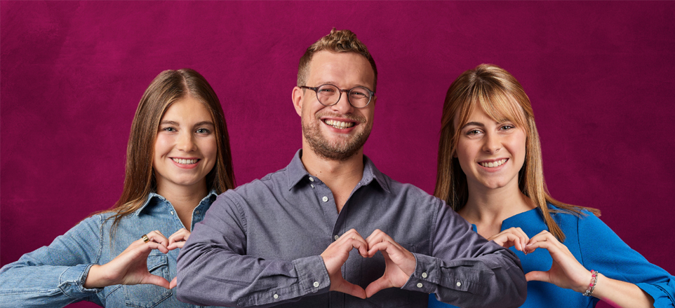 Drei Personen formen mit ihren Händen ein Herz und lächeln in die Kamera.