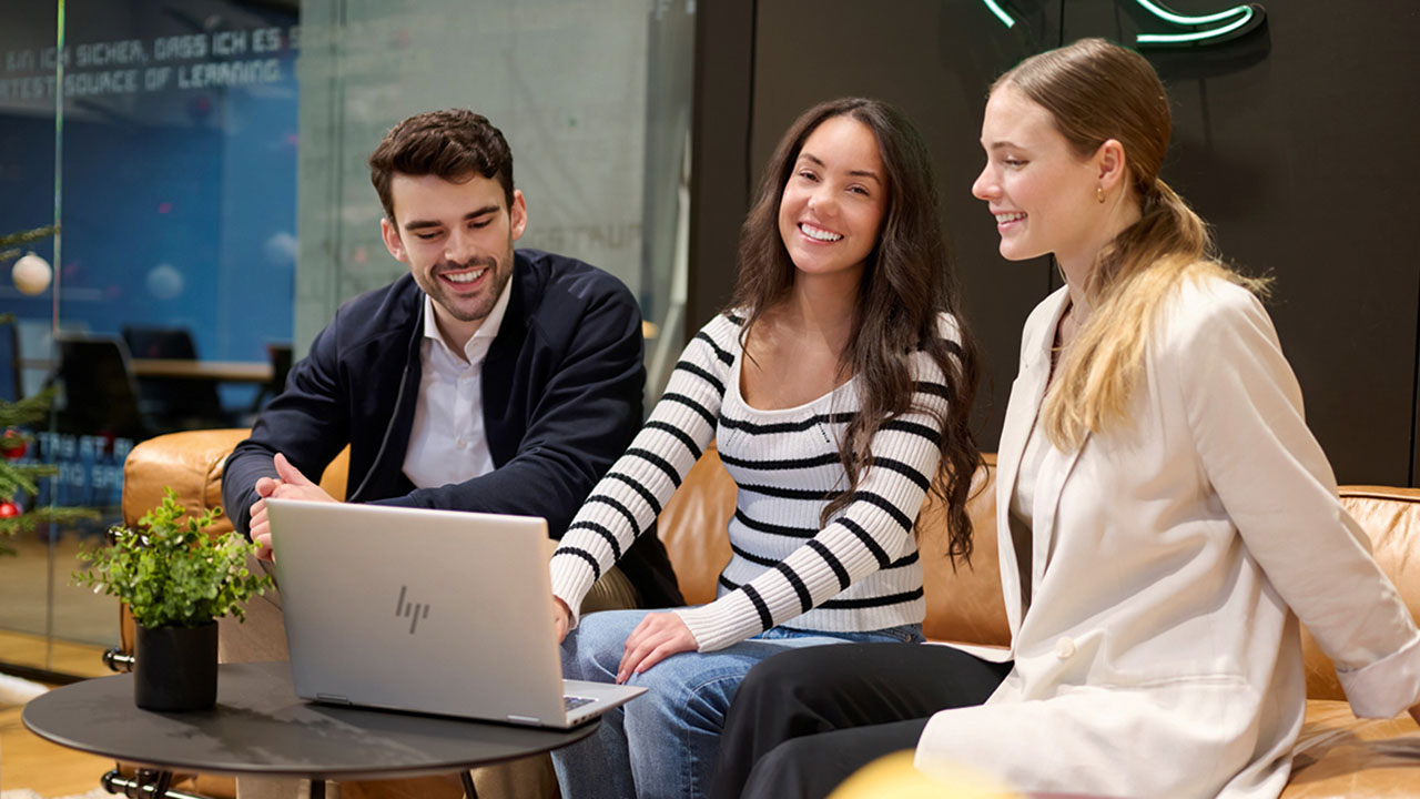 Drei junge lächelnde Personen sitzen vor einem Laptop