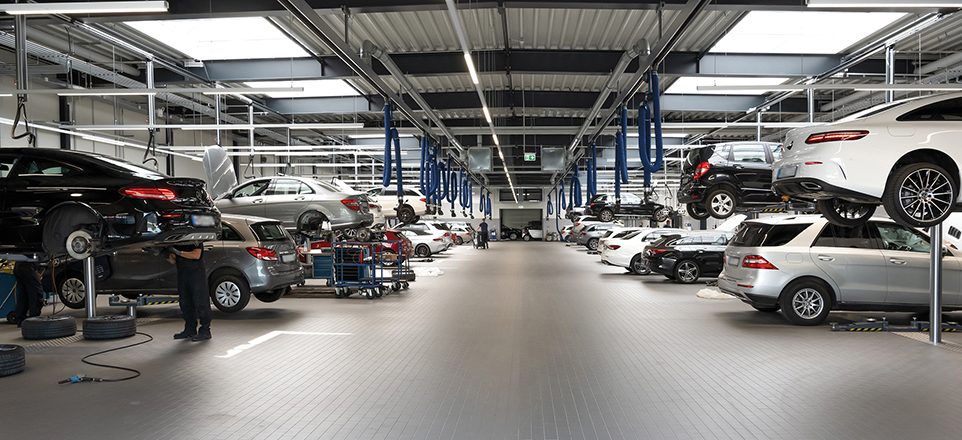 In einer großen Halle stehen viele Autos. Eine Person wechselt die Reifen eines Autos.