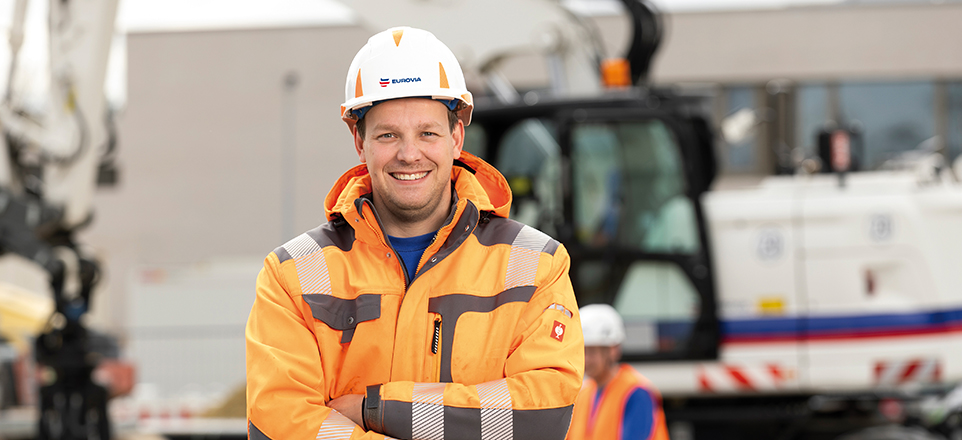 Mann in Arbeitskleidung und Arbeitshelm blickt in die Kamera