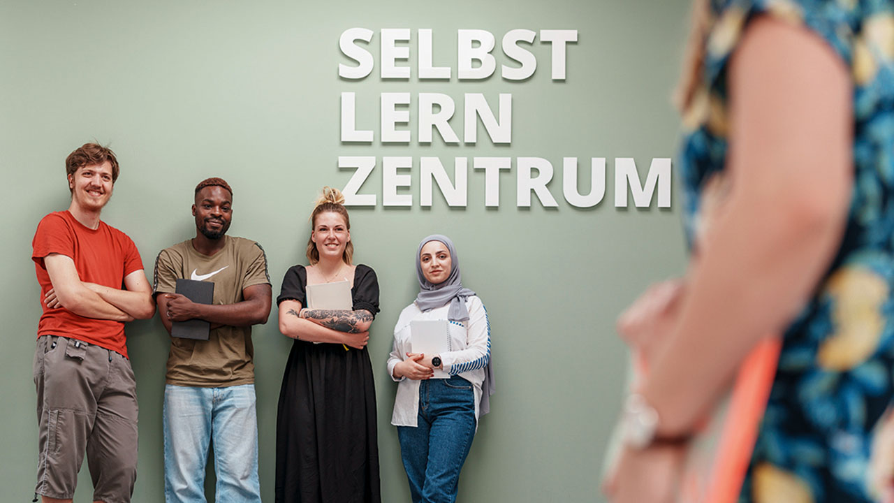 Studierende der Evangelischen Hochschule Rheinland-Westfalen-Lippe vor einer Wand mit der Aufschrift Selbstlernzentrum 