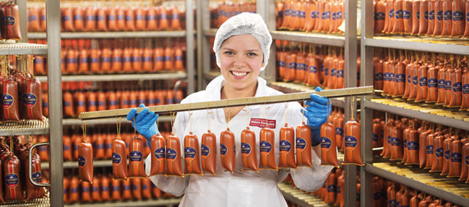 Eine Person hält mehrere Wurstwaren in den Händen in einem Räucherraum.