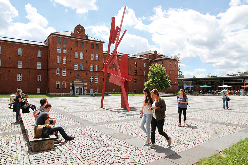 Hochschulgebäude mit roter Skulptur und einigen Studierenden.