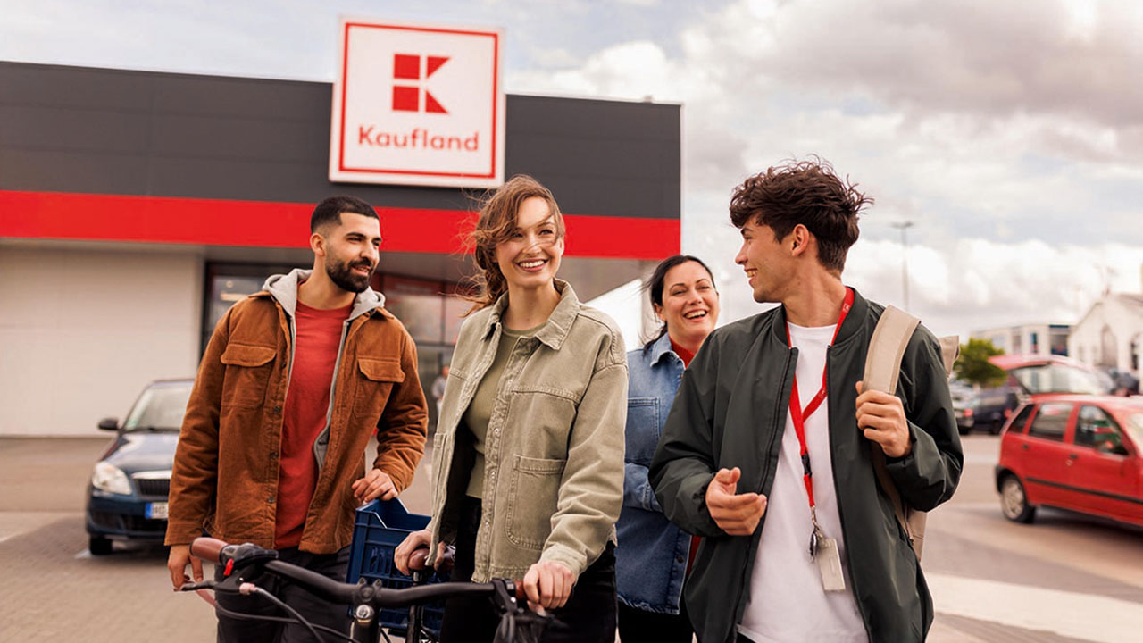 Vier junge lächelnde Personen auf dem Parkplatz vor einer Kaufland-Filiale