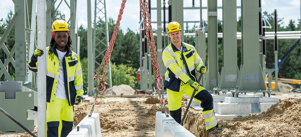 Zwei Personen in gelber Schutzkleidung mit Helm euf einer Baustelle