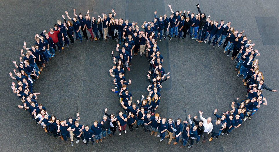Teamfoto von oben aufgenommen, Mitarbeitende bilden die zwei ineinander verschlungenen Ringe des Logos