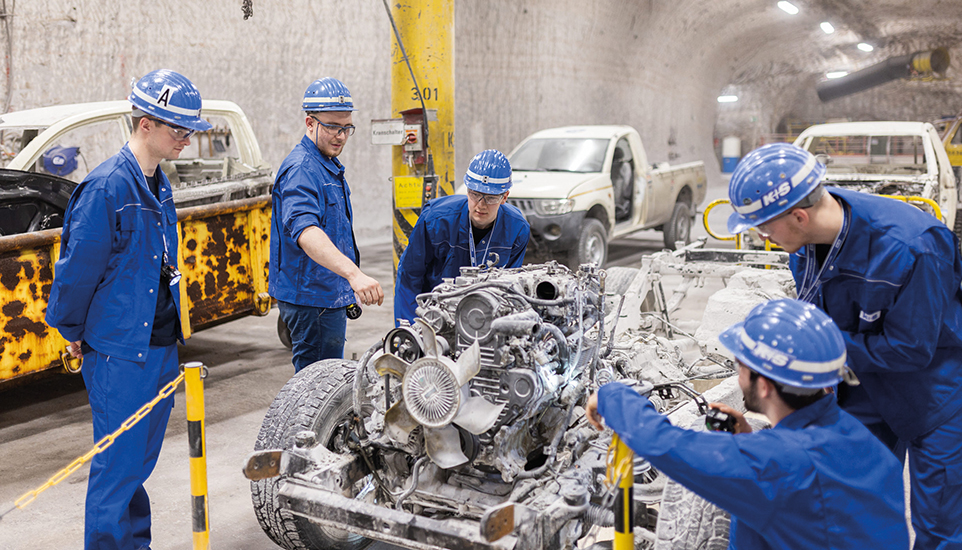 Personen imblauen Arbeitsanzügen und Helmen arbeiten an einem Auto in einem Salzstollen