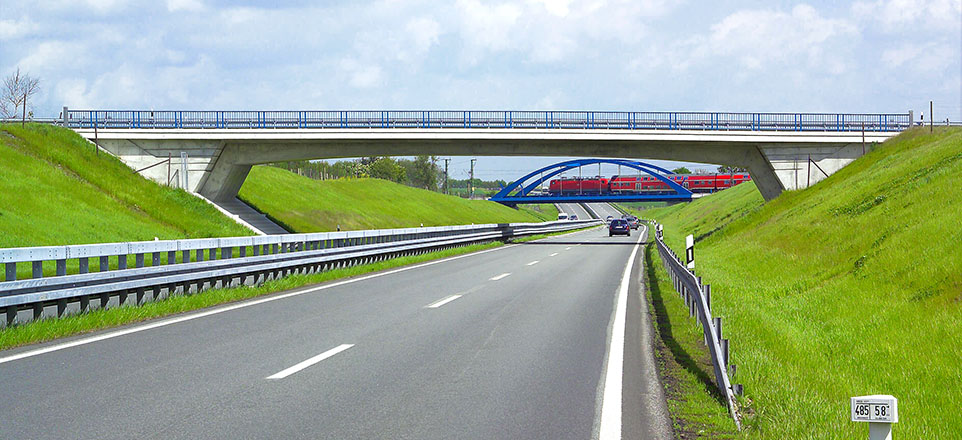 Aufnahme einer Straße. Diese führt unter einer normalen und einer Eisenbahnbrücke hindurch.
