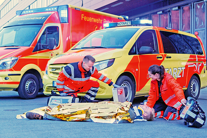 Personen versorgen Verwundeten vor einem Rettungswagen.