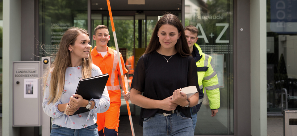 Personengruppe mit verschiedenen Werkzeugen und Geräten verlässt das Landratsamt Bodenseekreis.