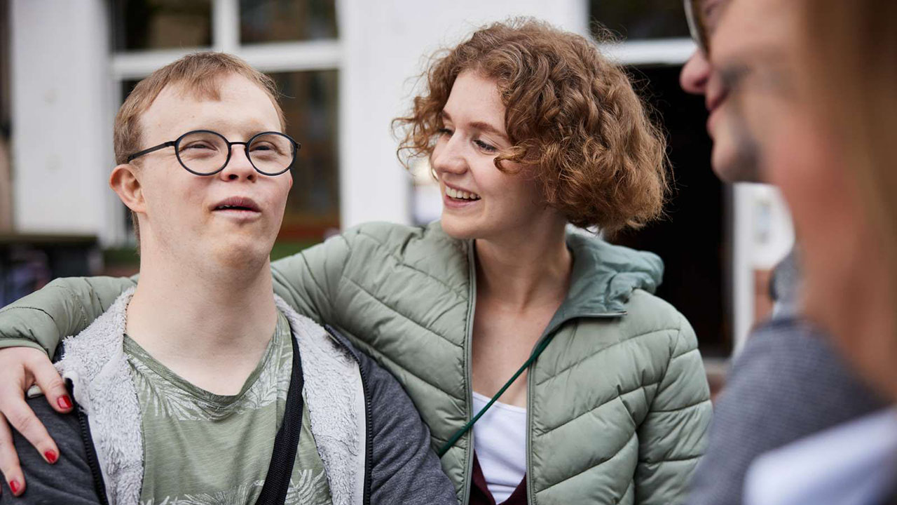 Person legt einen Arm um eine Person mit Brille