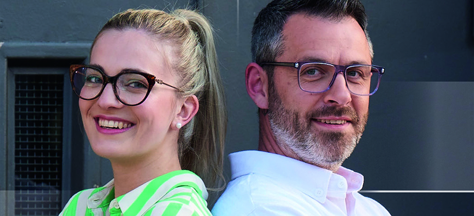 Zwei Personen mit Brille lächeln in die Kamera.