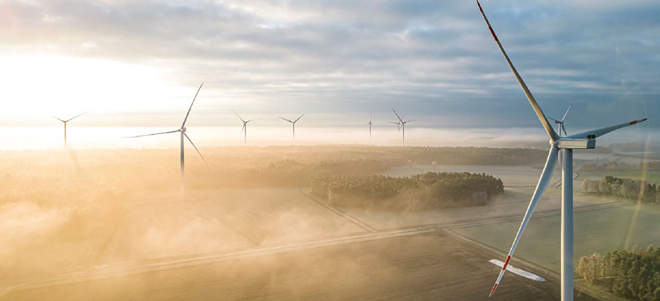 Windräder auf Feldern mit Sonneneinfall bei bewölktem Himmel