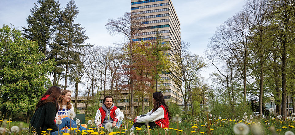 Vier Personen sitzen im Grünen, im Hintergrund die Radboud Universiteit Nijmegen.