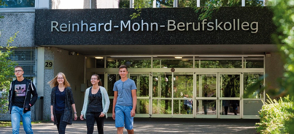 Vier Personen kommen lächelnd aus dem Reinhard-Mohn-Berufskolleg.