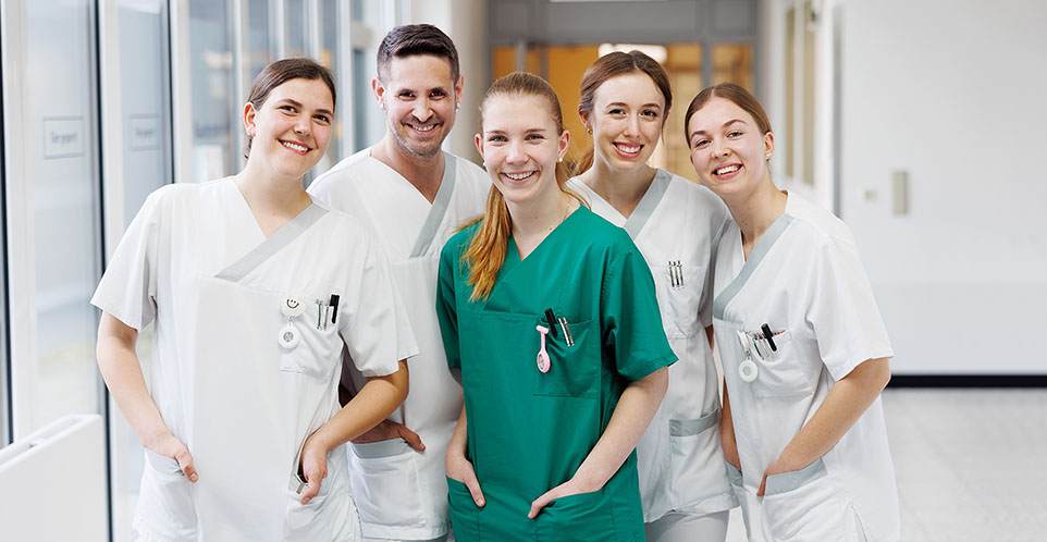 Mitarbeitende der Rems-Murr-Kliniken stehen im Krankenhausflur und lächeln in die Kamera.