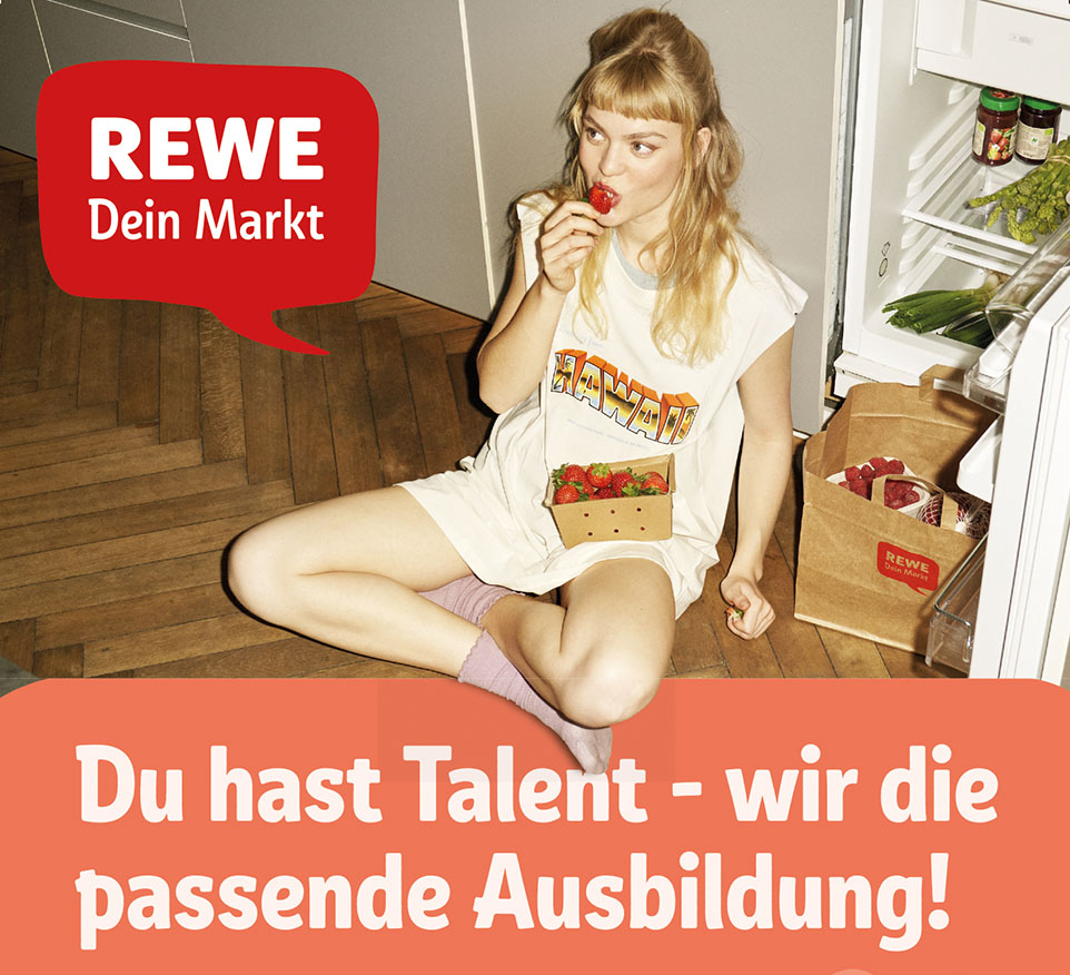 Junge Person sitzt mit einer Schale Erdbeeren vor dem Kühlschrank am Boden und beißt genüsslich in eine Erdbeere. Daneben steht der Slogan: Du hast Talent – wir die passende Ausbildung! / Logo REWE
