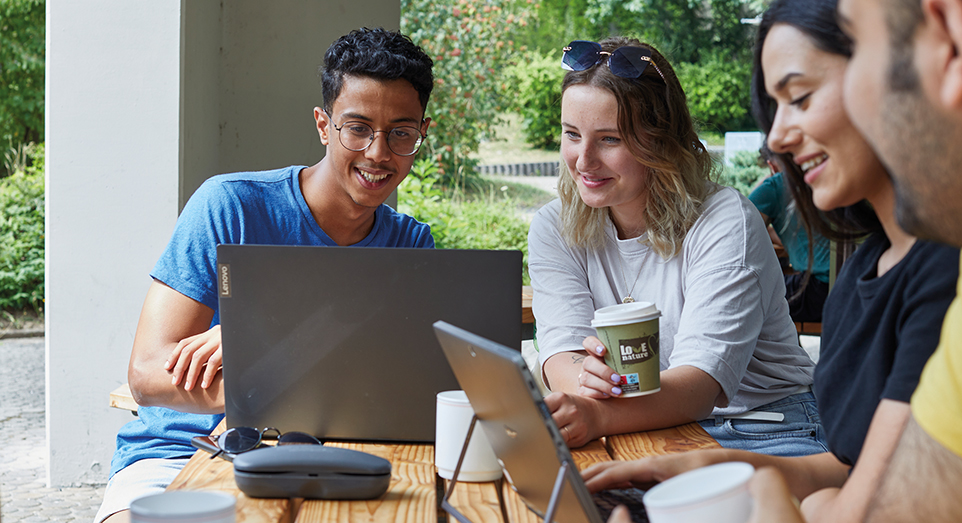 Vier Personen sitzen zusammen und sehen auf zwei Laptops.