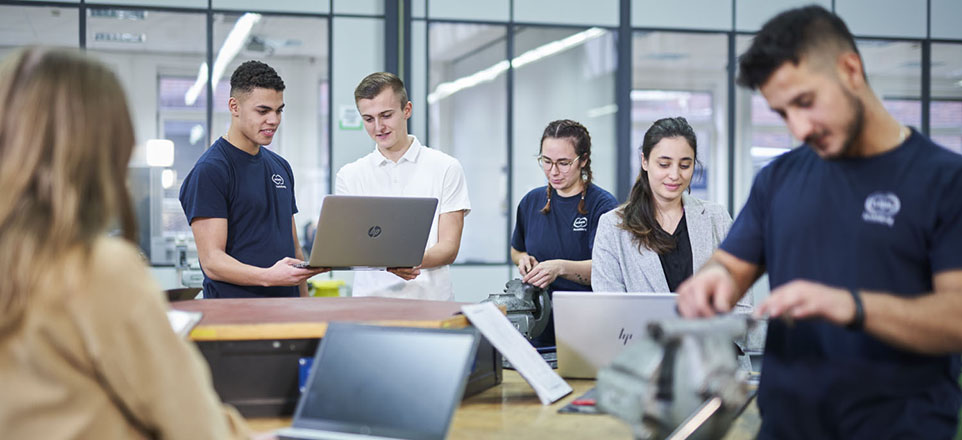 Vier Personen arbeiten an Computern und zwei Personen arbeiten an elektromechanischen Komponenten