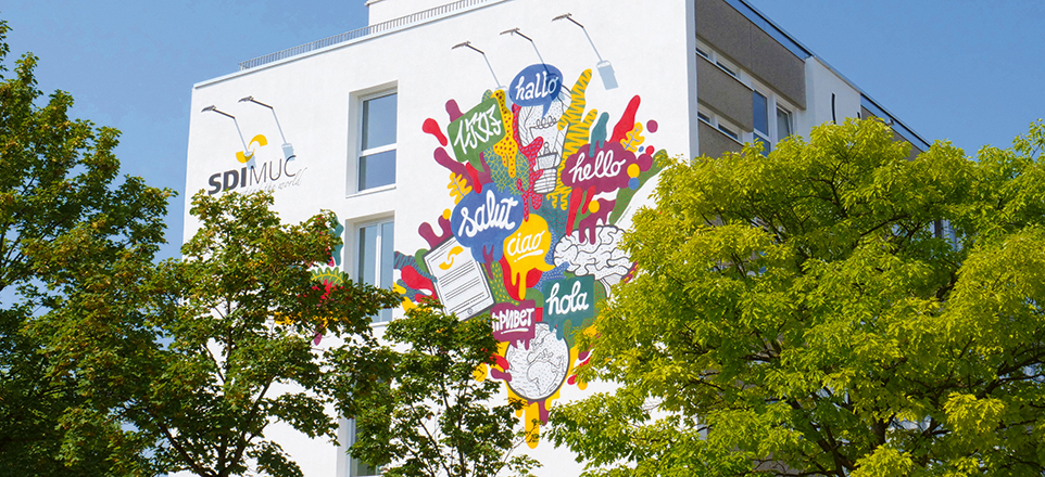 bunt angemaltes SDI Gebäude versteckt hinter Bäumen