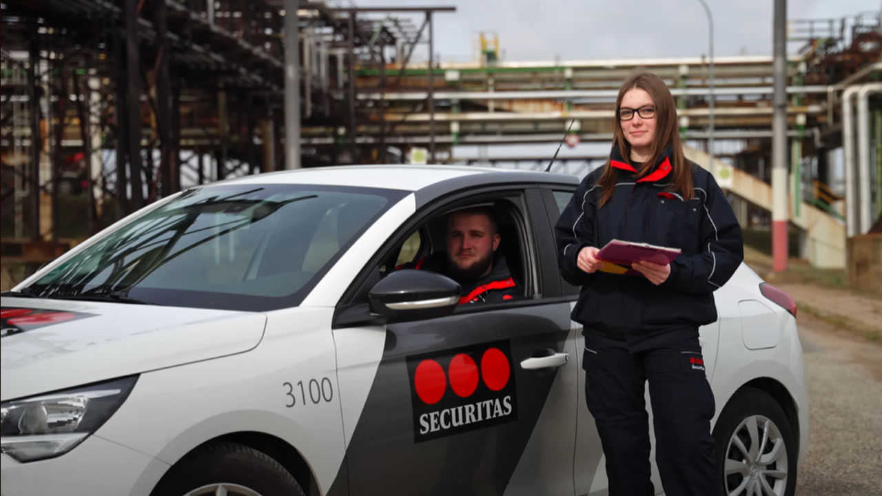 Zwei Mitarbeitende von Securitas, eine Person sitzt in einem Auto, eine weitere Person steht neben dem Auto