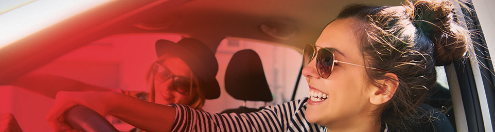Zwei junge lächelnde Personen mit Sonnenbrille fahren im Auto