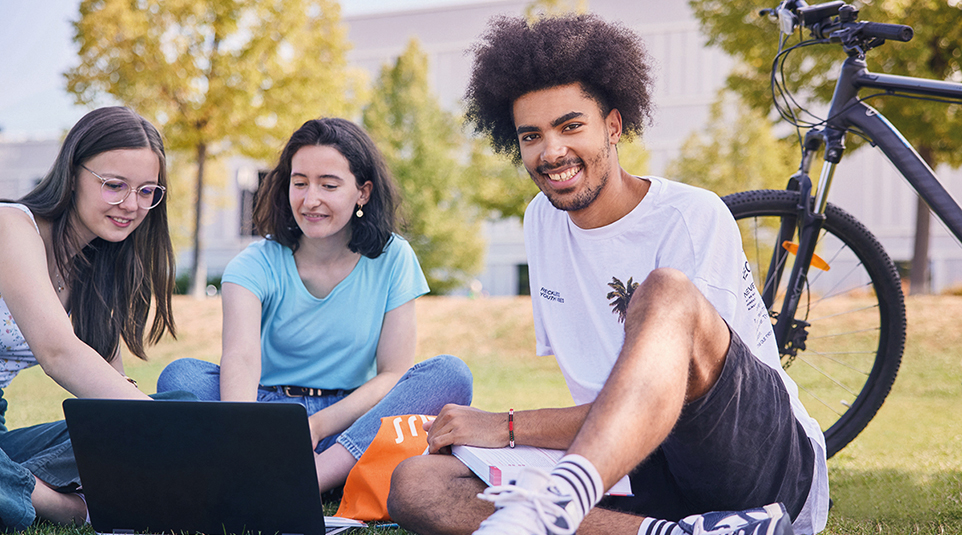 Kleine Gruppe junger Menschen sitzt im freien vor Laptop