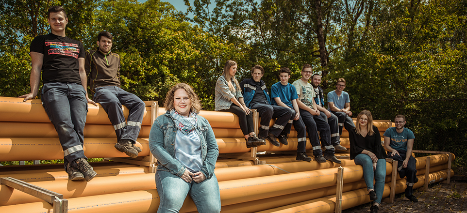 Gruppenbild, junge Menschen sitzen auf einer überdimensionalen Bank aus gelben Rohren