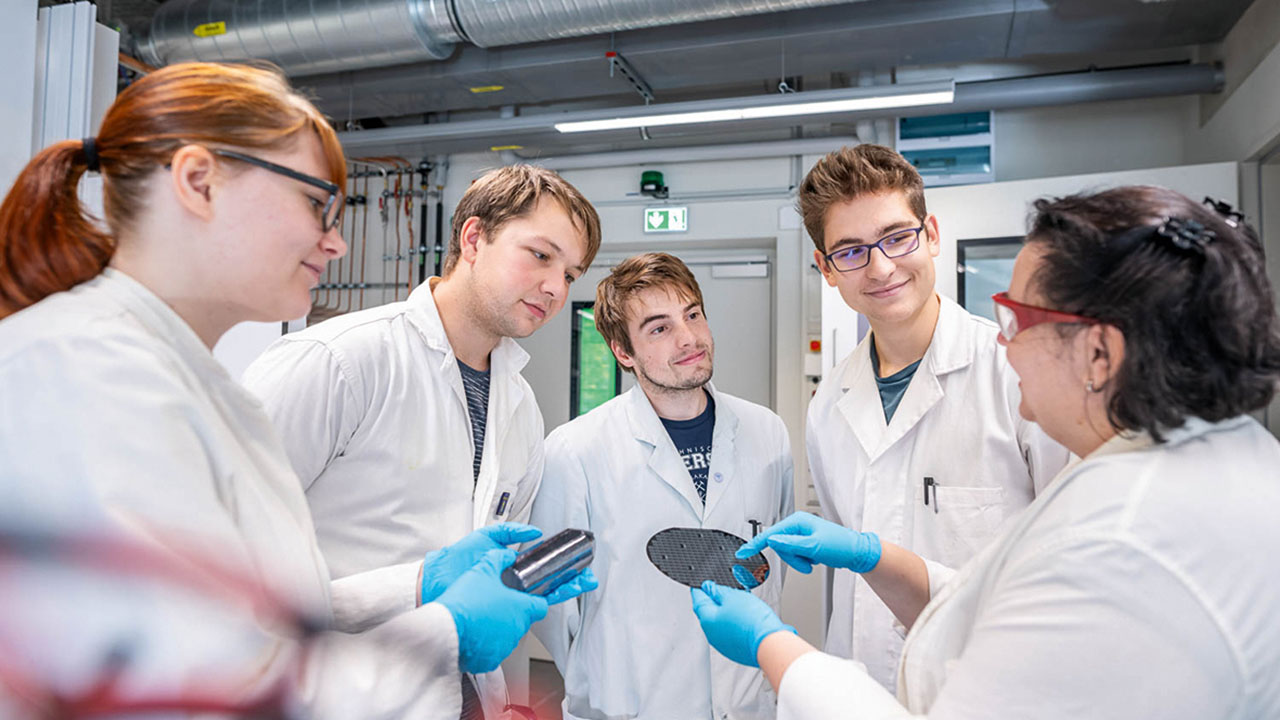 Vier Studierende und eine Lehrende in weißen Kitteln mit blauen Schutzhandschuhen