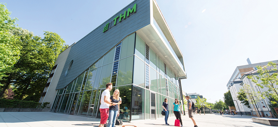 Junge Menschen stehen vor der Technischen Hochschule Mittelhessen und unterhalten sich. 