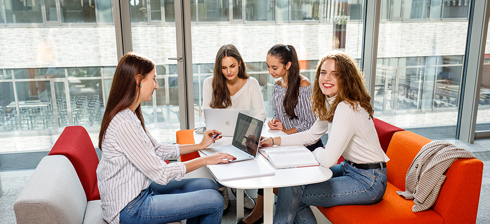 Vierer Personengruppe sitzt zusammen an einem Tisch und liest in Büchern.
